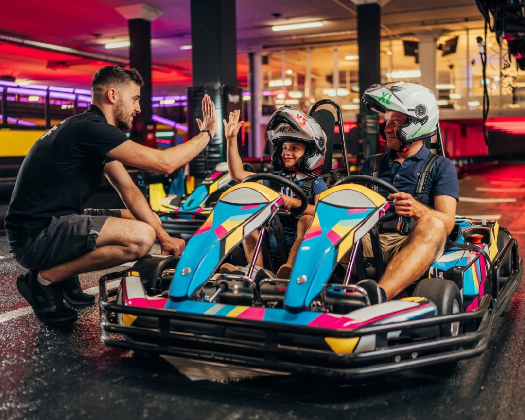 Staff high-fiving a young racer in a go-kart beside her dad