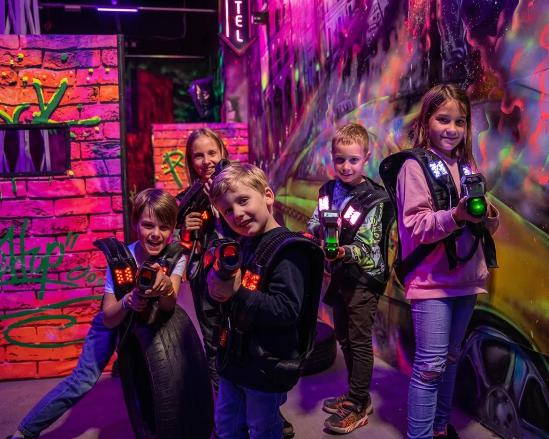 Kids in glowing vests posing with blasters in a laser tag arena